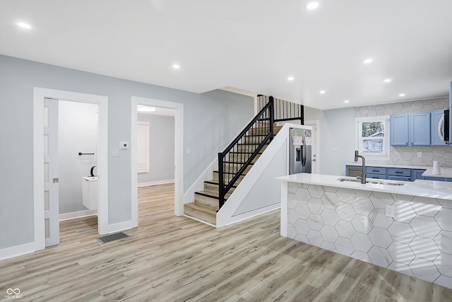 kitchen featuring tasteful backsplash, stainless steel refrigerator with ice dispenser, sink, light wood-type flooring, and blue cabinets