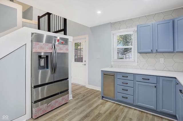 kitchen featuring backsplash, stainless steel refrigerator with ice dispenser, light wood-type flooring, and blue cabinets