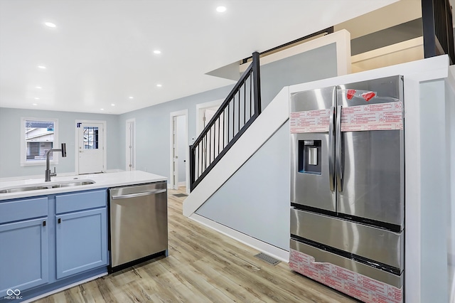 kitchen with sink, blue cabinetry, light wood-type flooring, and appliances with stainless steel finishes