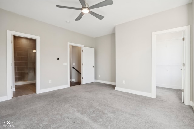 unfurnished bedroom with light carpet, ceiling fan, a spacious closet, a closet, and ensuite bath