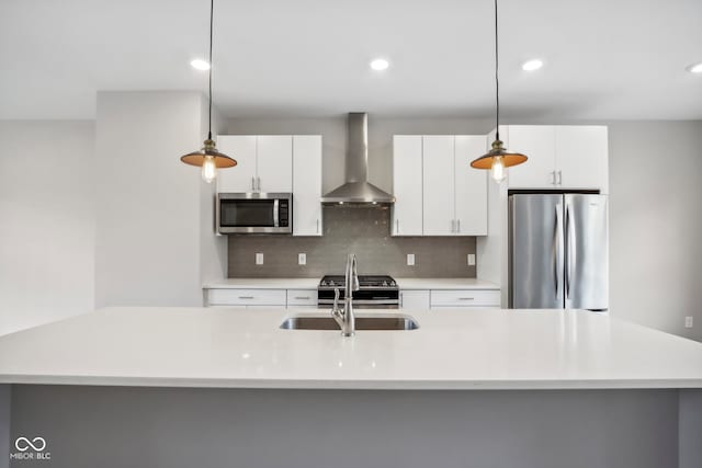 kitchen featuring appliances with stainless steel finishes, wall chimney exhaust hood, decorative light fixtures, and an island with sink