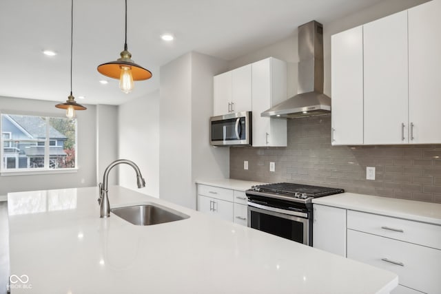 kitchen featuring wall chimney range hood, sink, appliances with stainless steel finishes, white cabinetry, and pendant lighting