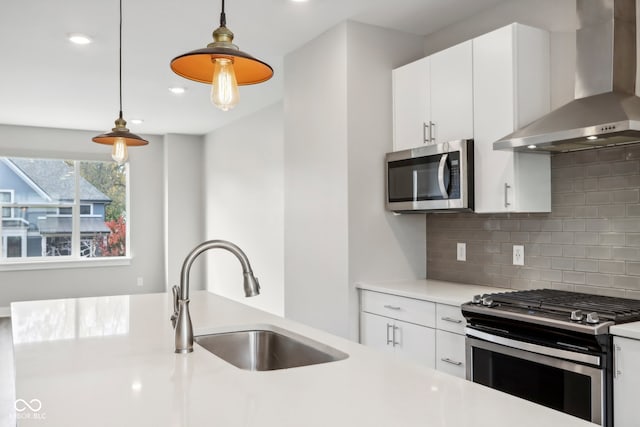 kitchen featuring wall chimney range hood, stainless steel appliances, sink, decorative light fixtures, and white cabinets