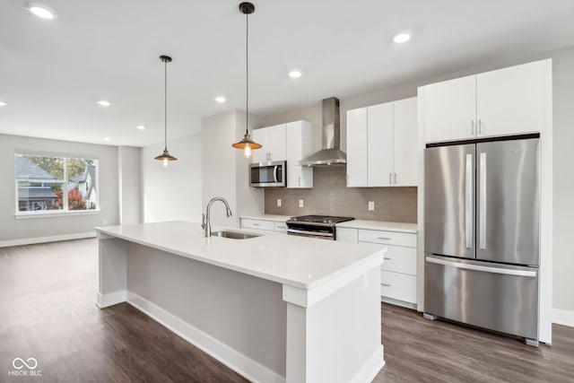 kitchen with wall chimney range hood, an island with sink, sink, pendant lighting, and appliances with stainless steel finishes