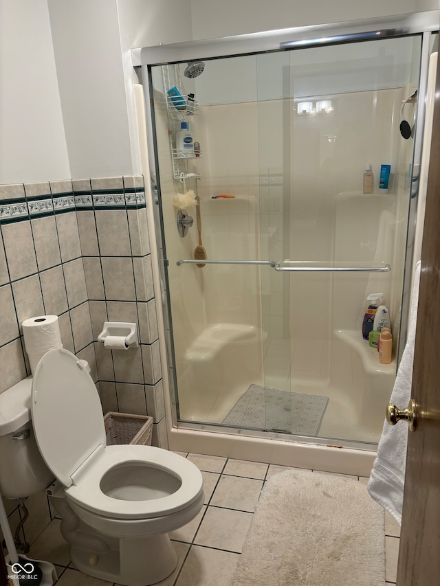 bathroom with a shower with door, tile walls, toilet, and tile patterned flooring