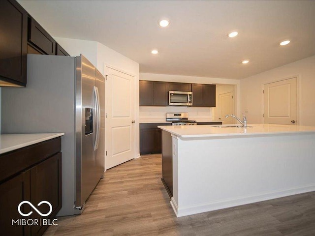 kitchen with sink, light hardwood / wood-style flooring, an island with sink, dark brown cabinetry, and stainless steel appliances