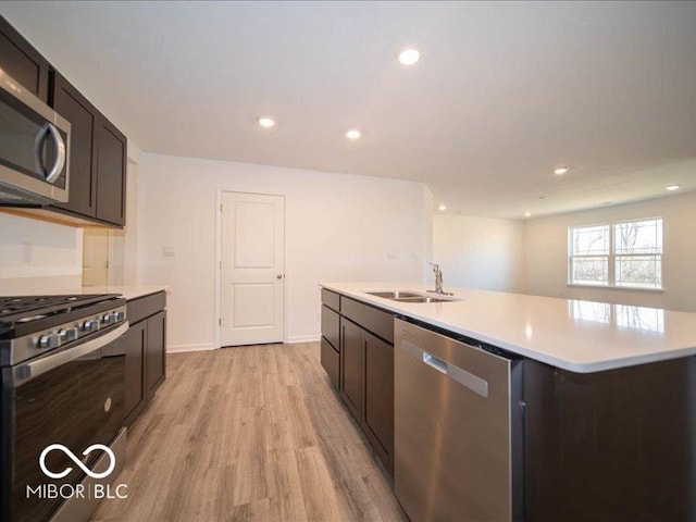 kitchen with a center island with sink, light wood-type flooring, sink, and appliances with stainless steel finishes