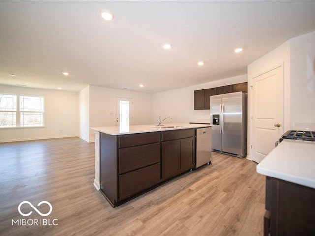 kitchen with a kitchen island with sink, sink, light hardwood / wood-style flooring, appliances with stainless steel finishes, and dark brown cabinets