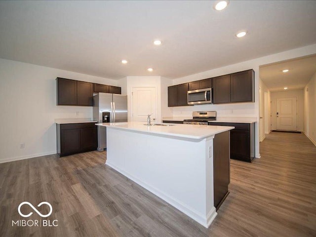 kitchen with sink, an island with sink, dark brown cabinets, wood-type flooring, and stainless steel appliances