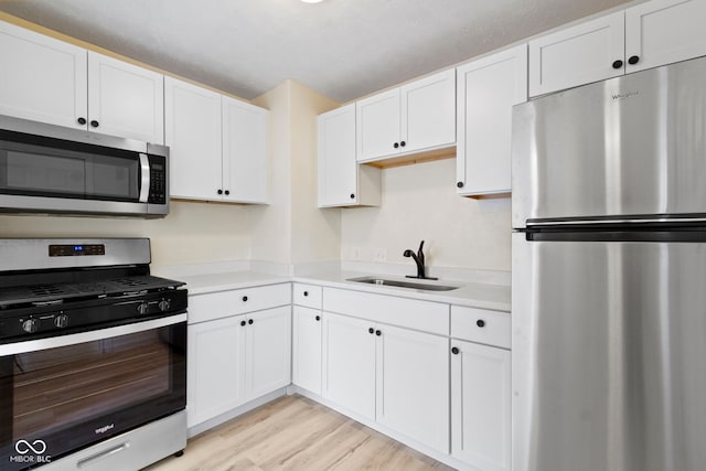 kitchen with sink, appliances with stainless steel finishes, light wood-type flooring, and white cabinets