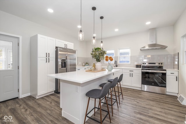 kitchen with stainless steel appliances, a kitchen island, white cabinets, dark wood-type flooring, and wall chimney exhaust hood