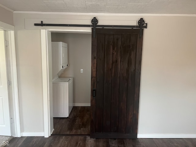 washroom with dark wood-type flooring, stacked washer and clothes dryer, crown molding, and a barn door