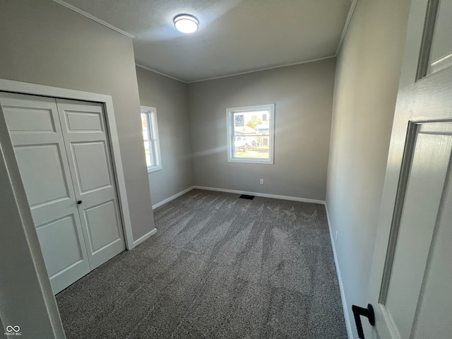 unfurnished bedroom with a textured ceiling, a closet, crown molding, and dark carpet