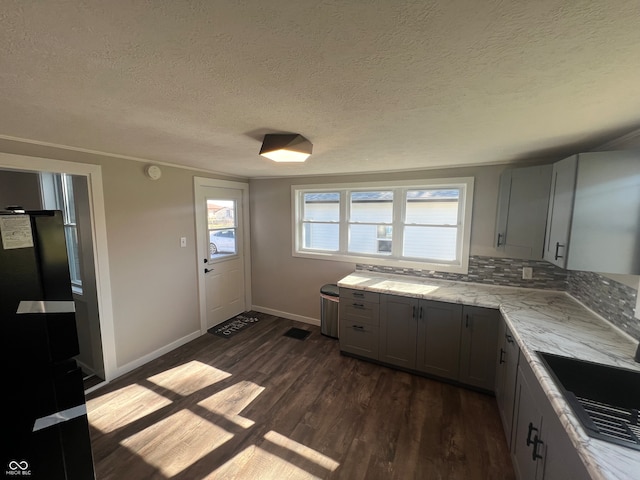 kitchen featuring gray cabinets, tasteful backsplash, dark wood-type flooring, light stone countertops, and a textured ceiling