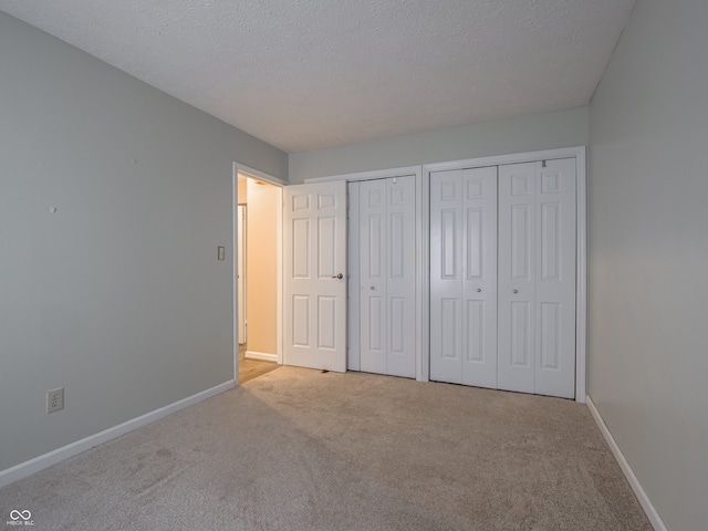 unfurnished bedroom with light colored carpet, a textured ceiling, and two closets