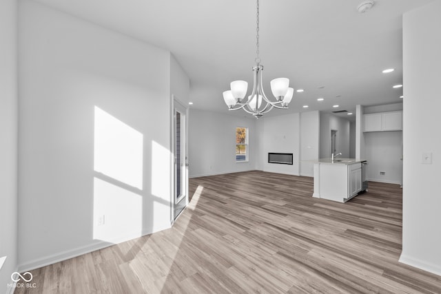 unfurnished living room featuring an inviting chandelier, sink, and light hardwood / wood-style flooring