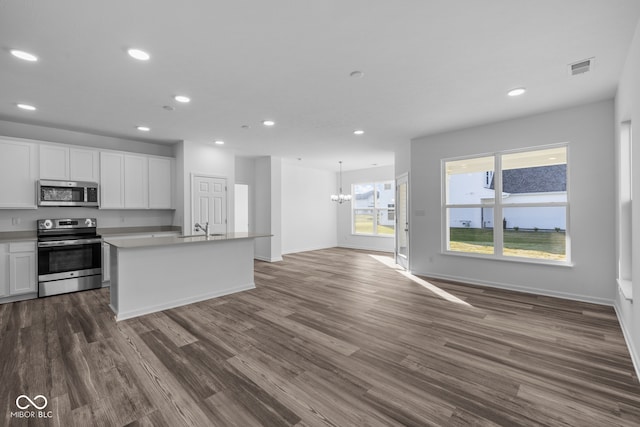 kitchen with a center island with sink, stainless steel appliances, an inviting chandelier, white cabinets, and dark wood-type flooring