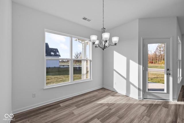 unfurnished dining area with an inviting chandelier, a wealth of natural light, and wood-type flooring