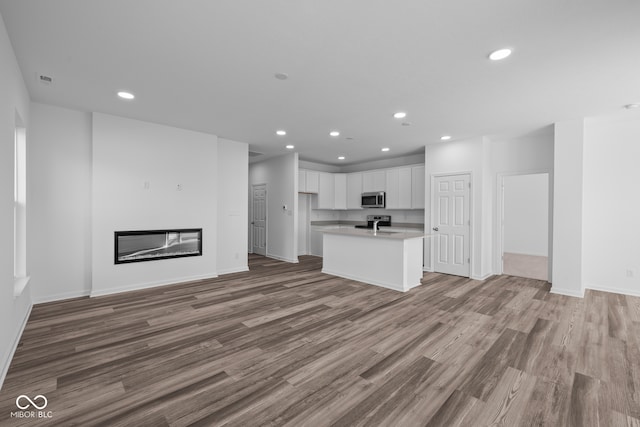 kitchen with stainless steel appliances, wood-type flooring, white cabinets, and an island with sink