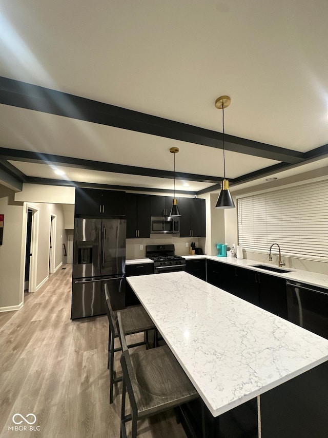 kitchen featuring light wood finished floors, appliances with stainless steel finishes, dark cabinets, beam ceiling, and a sink