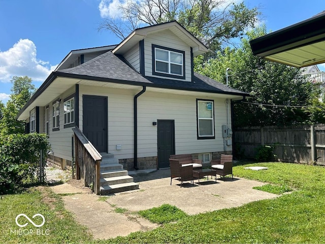 back of house with entry steps, fence, roof with shingles, a lawn, and a patio area