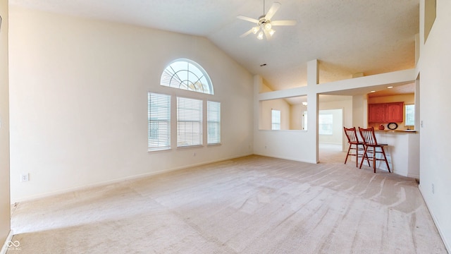 unfurnished living room featuring ceiling fan, high vaulted ceiling, and light colored carpet