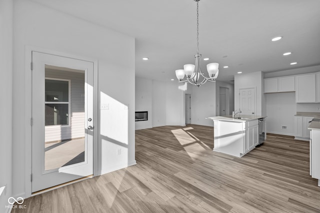 kitchen featuring hanging light fixtures, sink, a kitchen island with sink, white cabinetry, and light hardwood / wood-style flooring