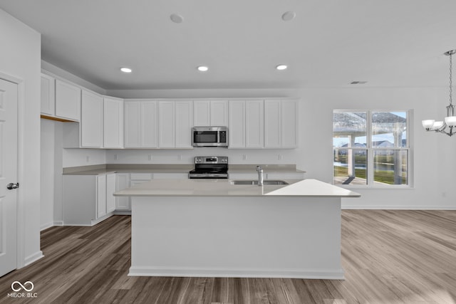 kitchen with stainless steel appliances, hanging light fixtures, a kitchen island with sink, white cabinets, and light wood-type flooring