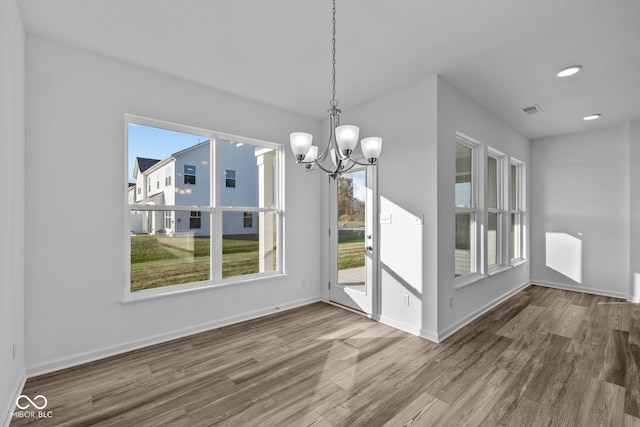 unfurnished dining area featuring a wealth of natural light, wood-type flooring, and a notable chandelier