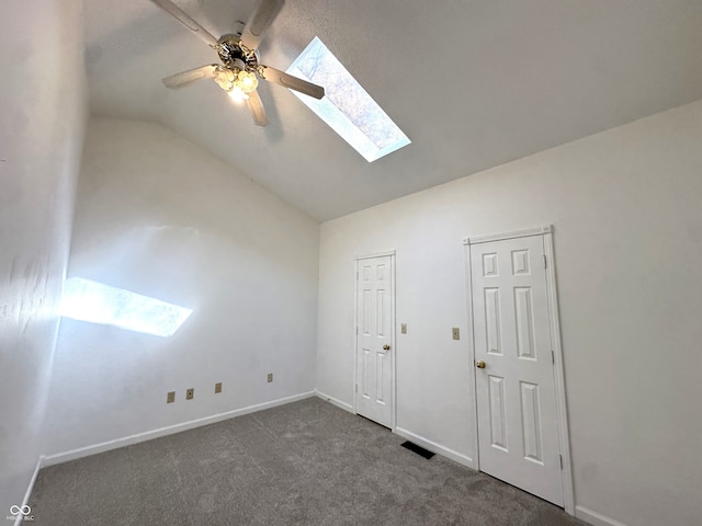 unfurnished bedroom with dark carpet, vaulted ceiling with skylight, multiple windows, and ceiling fan