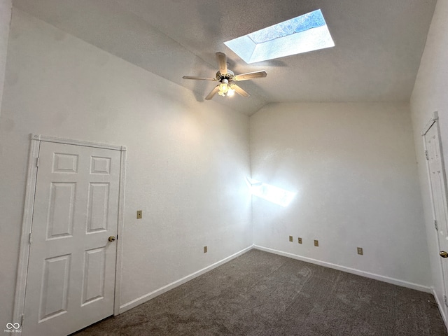 empty room featuring lofted ceiling with skylight, dark colored carpet, and ceiling fan