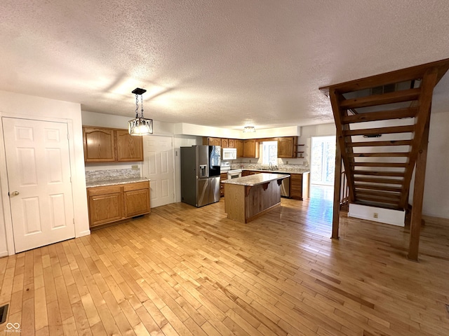 kitchen featuring appliances with stainless steel finishes, light wood-type flooring, a kitchen island, a textured ceiling, and decorative light fixtures