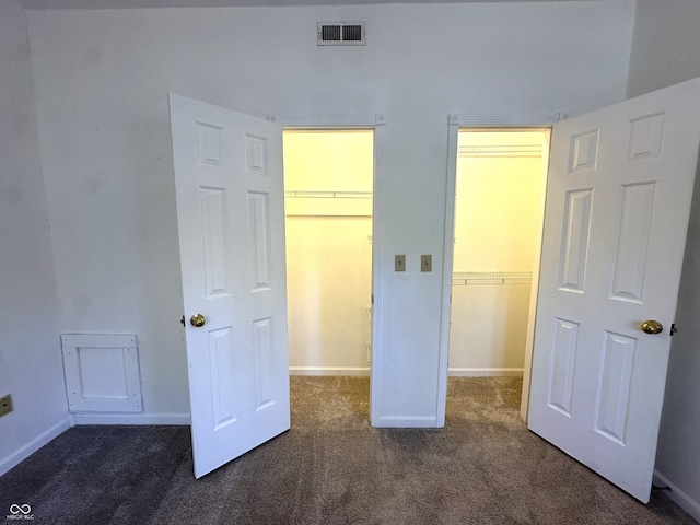 unfurnished bedroom with a closet, dark colored carpet, and a walk in closet