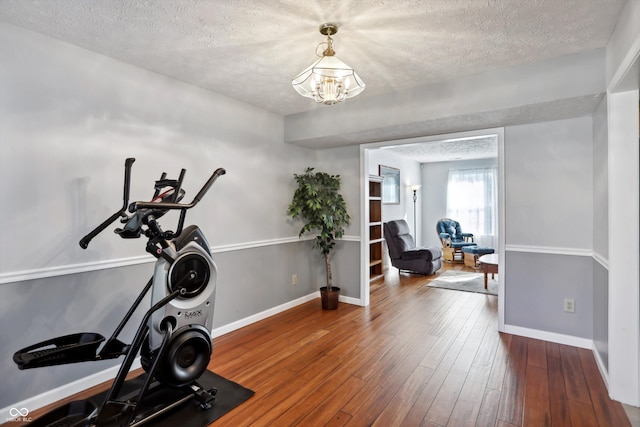 exercise room with a notable chandelier, hardwood / wood-style floors, and a textured ceiling