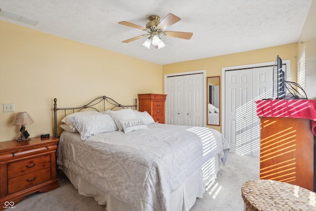 carpeted bedroom featuring multiple closets, a textured ceiling, and ceiling fan