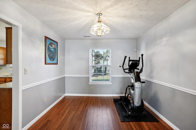 exercise room featuring dark wood-type flooring, a notable chandelier, and a textured ceiling