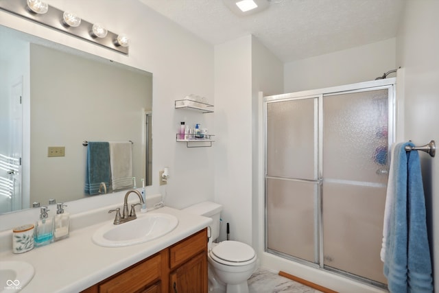 bathroom featuring vanity, toilet, a textured ceiling, and a shower with shower door