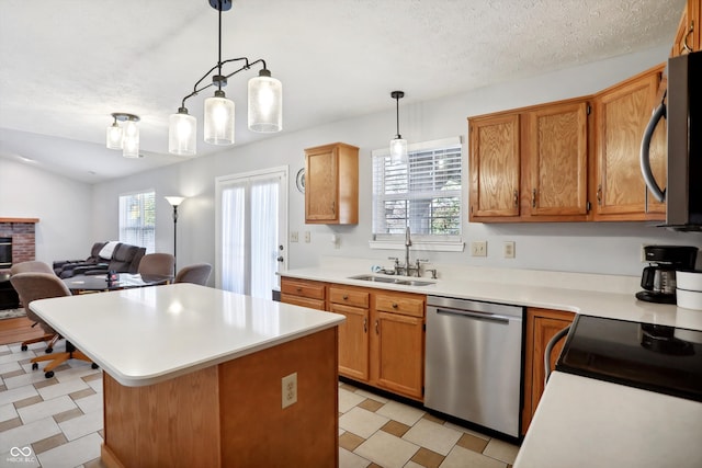 kitchen with appliances with stainless steel finishes, sink, a fireplace, a textured ceiling, and hanging light fixtures