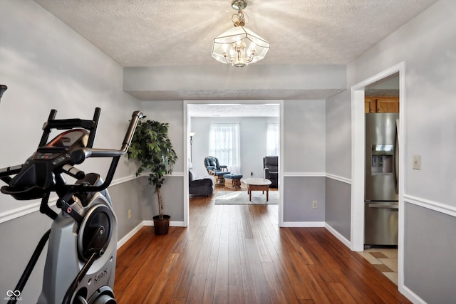 workout area with a notable chandelier, a textured ceiling, and dark wood-type flooring