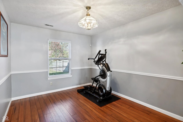 exercise area featuring a textured ceiling, an inviting chandelier, and hardwood / wood-style floors