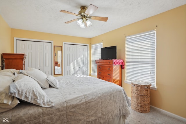 bedroom with a textured ceiling, multiple closets, carpet flooring, and ceiling fan