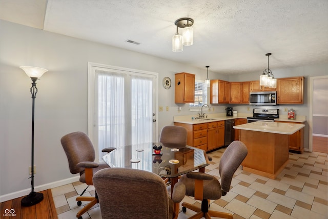 kitchen with hanging light fixtures, a kitchen island, a textured ceiling, sink, and stainless steel appliances