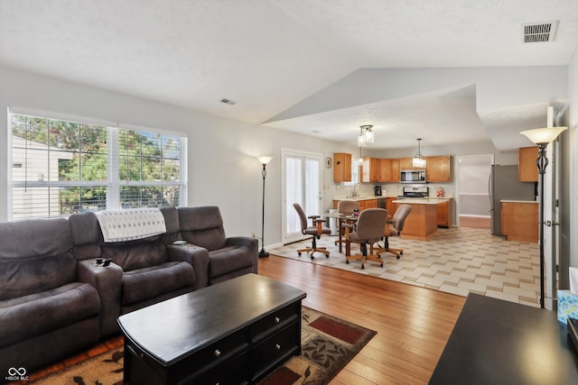 living room featuring sink, light hardwood / wood-style floors, a textured ceiling, and lofted ceiling