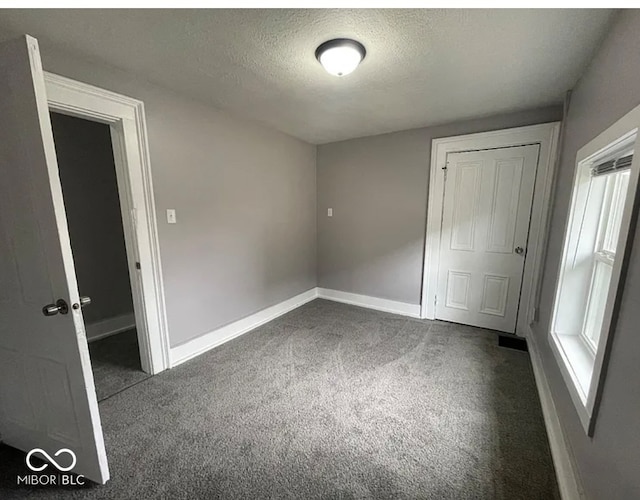 unfurnished bedroom featuring dark carpet, a textured ceiling, and a closet