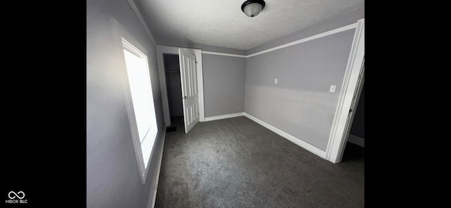 interior space featuring ornamental molding, dark colored carpet, and a textured ceiling