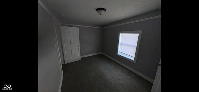 spare room featuring crown molding and dark carpet