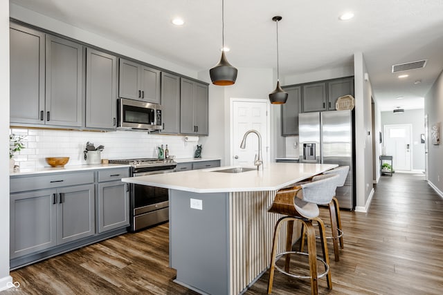 kitchen featuring a kitchen island with sink, sink, pendant lighting, gray cabinets, and stainless steel appliances