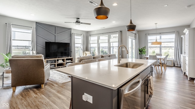 kitchen featuring sink, light wood-type flooring, an island with sink, dishwasher, and ceiling fan