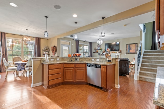 kitchen featuring stainless steel dishwasher, a center island with sink, decorative light fixtures, and light wood-type flooring