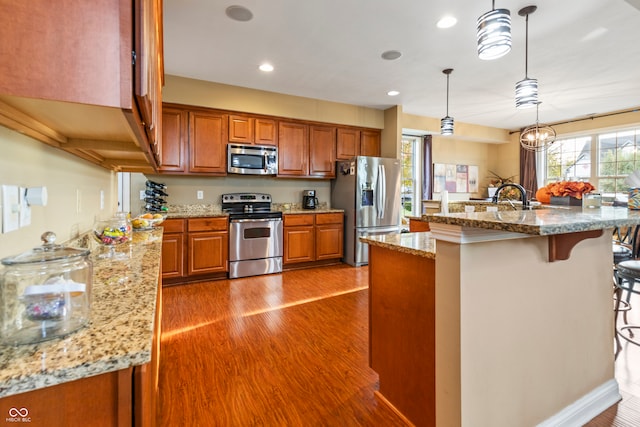 kitchen with stainless steel appliances, a kitchen island with sink, a breakfast bar, light stone countertops, and pendant lighting